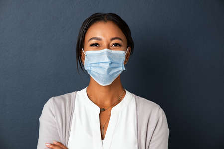 Beautiful young mixed race woman wearing protective face mask isolated against grey wall with copy space.の写真素材