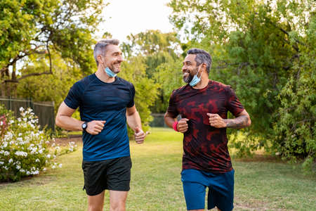 Two mature men running in park with protective face mask during lockdownの写真素材