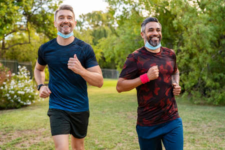 Two mature men running in park with protective face mask during lockdownの写真素材