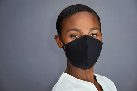 Beauty mature black woman wearing protective face mask isolated against grey wall. African american entrepreneur wearing face maskの写真素材