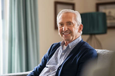 Portrait of happy senior man smiling at home. Old man in casual relaxing on sofa and looking at camera. Portrait of elderly man enjoying retirement at nursing home.の写真素材