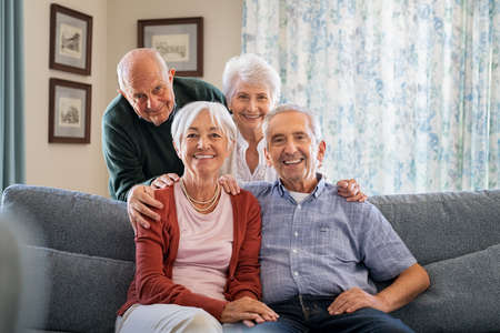 Portrait of happy elderly people on couch at care centre looking at camera. Senior couple posing for a photo sitting on couch in nursing home. Cheerful old man and beautiful woman looking at camera with copy space.の写真素材