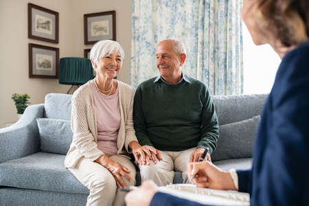 Medical advisor during home visit with senior couple. Financial insurance agent holding clipboard and writing notes in conversation with old couple at home. Business agent planning with a retired couple their future investment opportunities.の写真素材