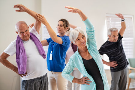Active seniors doing exercise with physiotherapist at nursing home gym. Trainer helping elderly man and old woman exercising at home. Retired people doing stretching exercises at retirement community.の写真素材