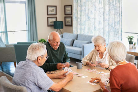 Happy senior people playing cards together at retirement community. Retired group of senior couples playing cards at care centre. Cheerful active seniors enjoying afternoon together at nursing home.の写真素材