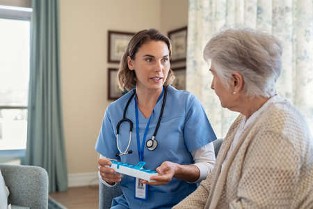 Young nurse explaining medicine dosage to old patient in care facility centre while holding weekly medicine dispenser. Professional caregiver holding pill organizer box giving medicine tablet to elderly woman. Nurse explaining medicine daily dosage for senior woman at care centre with copy space.の写真素材
