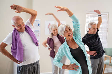 Group of seniors doing stretching exercise together at retirement centre. Elderly men and old women exercising at nursing home during daily fitness. Retired couples exercising at care facility.の写真素材