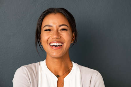 Close up face of beautiful mature woman looking at camera with big laugh. Mid adult hispanic woman standing isolated against grey wall while looking at camera. Portrait of smiling indian lady laughing on gray background.の写真素材