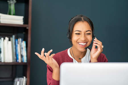 Portrait of smiling african mature woman doing video call using laptop. Mid adult african businesswoman with headset talking during online meeting with colleague. Indian happy woman working from home over a video conference on computer.の写真素材