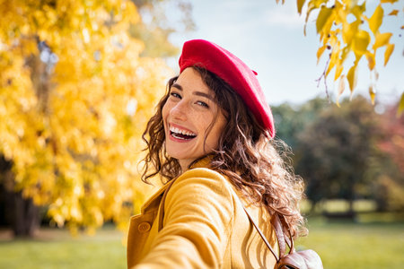 Happy casual girl holding hand and looking behind while walking in the park. Beautiful natural woman...