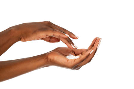 Close up of female african woman applying organic cream on hand. Detail of hands of ethnic woman with hand lotion isolated against white background. Side view of black hands with beauty cream: skin care and manicure concept.の写真素材
