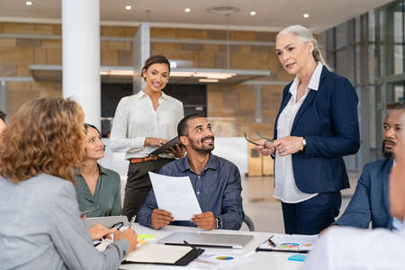 Group of mixed race business people discussing work in conference room. Senior business manager guiding employees in meeting. Group of businessman and businesswoman working together while brainstorming and sharing new ideas and strategy.の写真素材