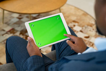 African business man using digital tablet with green screen for internet and email. Close up of hands of mature businessman using digital tablet with chroma key screen for video call. Back view of manager holding laptop with empty screen while typing on it.の写真素材