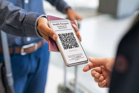 Close up hand of mixed race man showing health passport to flight attendant on phone. Hostess checking electronic vaccination proof at boarding gate. Airport check in counter and Covid-19 proof of vaccination control.の写真素材