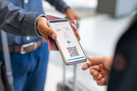 Close up hand of mixed race man showing electronic boarding pass to flight attendant on phone. Hostess checking electronic flight ticket at boarding gate. Airport check in counter and online air ticket.の写真素材