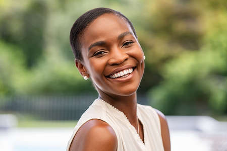 Portrait of smiling middle aged african woman looking at camera. Cheerful black mid adult woman smiling outdoor. Close up face of beautiful black lady laughing at park.の写真素材