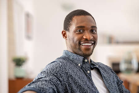 Portrait of middle aged african american man relaxing on couch at home. Handsome black mid adult man in casual clothing sitting on sofa and looking at camera. Successful mature guy stay at home with copy space.の写真素材