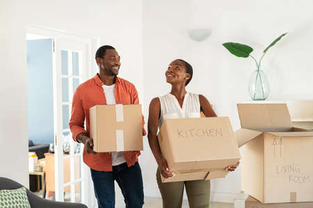 Happy african american man and beautiful woman holding cardboard boxes during moving house. Newly wed married black couple shifting home. Excited middle aged couple holding cardboard boxes while moving to new home.の写真素材