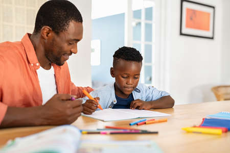 Mid black father helping his son with homework. African american boy studying with dad at home. Cute little child doing homework and studying with the help of his mature dad.の写真素材