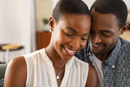 Beautiful mature woman with affectionate handsome black man at home. Romantic husband and smiling wife embracing while relaxing at home. Portrait of happy african american couple in love embracing at home: love and trust concept.の写真素材
