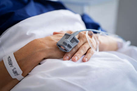 Close up of patient's hand in hospital with saline solution tube intravenous, iv drip. Close up of wrinkled hand of senior woman hospitalized and undergoing treatment at private clinic. Detail of pulse oximeter on index to measure blood oxygen saturation in hospital.の写真素材