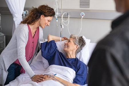 Lovely daughter and careful son visiting sick mother in hospital. Senior patient smiling in conversation with her family while hospitalized. Daughter visiting and cheering her old smiling mother lying in bed at hospital ward.の写真素材