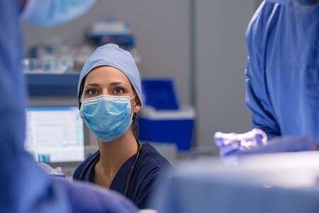 Nurse with a team of experienced doctor performing surgery on patient in operation theatre. Anesthetist in operating room following instructions given by surgeon. Young woman doctor with surgical mask and cap in operation theatre with team.の写真素材