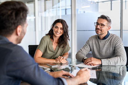 Smiling mature couple meeting with bank manager for investment. Beautiful mid adult woman with husband listening to businessman during meeting in conference room in modern office. Happy middle aged couple meeting loan advisor to buy a new home.の写真素材