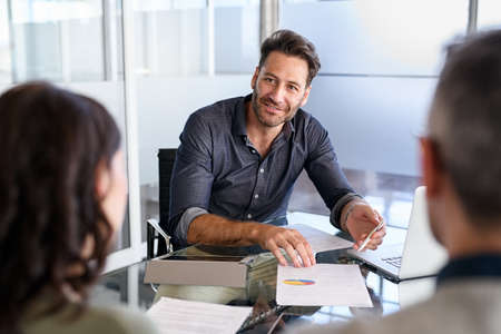 Mature financial agent in meeting sitting with mid adult couple to propose a new investment. Happy consultant talking with man and woman about their savings plan. Insurance advisor in a meeting with married couple asks for a mortgage.の写真素材