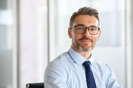 Portrait of successful business man with eyewear in office. Happy and smiling businessman standing in office while looking at camera with copy space. Portrait of handsome mature man in a modern workplace.の写真素材