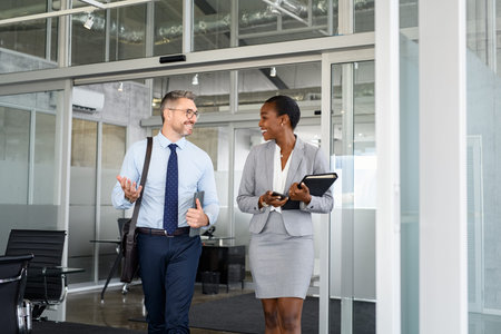 Smiling mature business man and african american businesswoman walking out of office. Two happy...