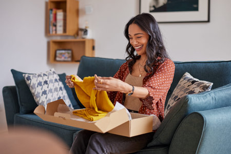 Happy young latin woman checking clothes at home. Cheerful shopaholic hispanic woman checking...