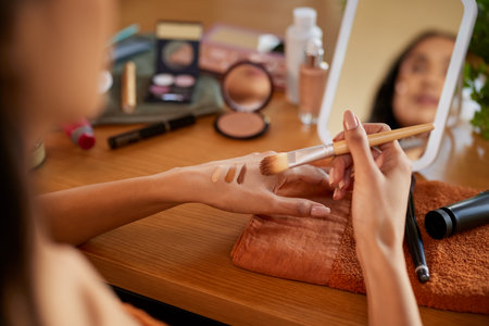 Close up of hands of young mixed race woman applying different shades of foundation on hand before makeup. Latin girl testing skin tone complexion on hand. Detail hands of mexican woman applying liquid foundation and mixing colors while preparing for the date.の写真素材