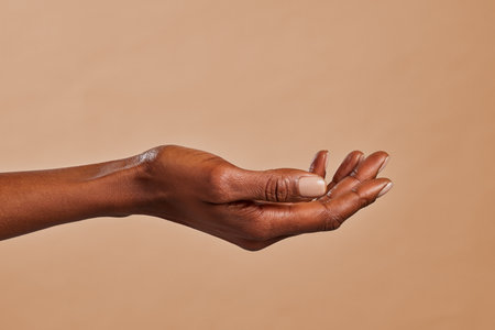 Close up of african american woman hand with palm facing upwards isolated on brown background. Female black hand showing empty hand. African girl holding your beauty product.の写真素材