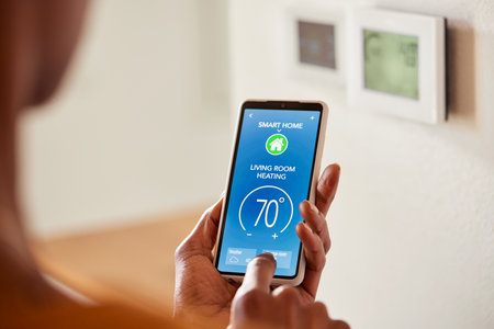 Close up of black female hand setting temperature of air conditioner or heat pump using smartphone at home. Back view of african american woman use smart home control app on phone in living room to adjust temperature and ventilation. Remote control of air conditioners, concept of energy efficiency, savings and ecology.の写真素材