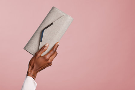 Female black hand holding elegant silver bag against red background. Hands of african american glamor woman holding purse isolated isolated with copy space. Fashion girl showing her new stylish clutch purse purchased during the sales.の写真素材