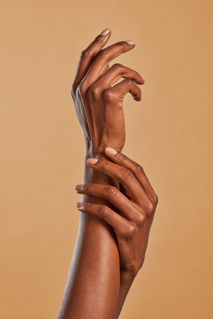 African american woman hands applying moisturizing cream. Black woman beauty gesturing with hands isolated on brown background. Female elegant hands touch each other with a movement of lightness.の写真素材