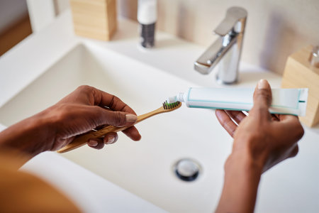 Black woman hand squeezing whitening paste on wooden toothbrush, taking care about mouth hygiene....
