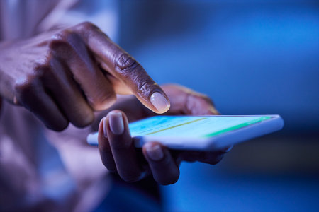 Close up of female african american hand using mobile phone in dark. Hands of black woman using smart phone during night. Woman texting on smartphone late in the evening.の写真素材