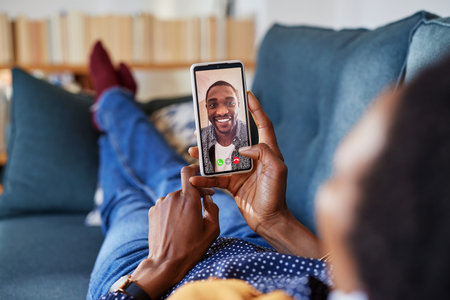 African american woman enjoying video call using smartphone with boyfriend while relaxing on couch....