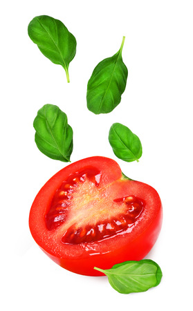Section of juicy tomato with falling green leaves of basil isolated on white backgroundの写真素材