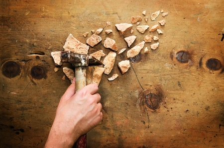 Men's hand takes a hammer and breaks a stone. Rustic vintage style. Top view. Creative concept background.の写真素材