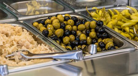 ingredients at a falafel bar with metal vegetable tongs green peppers black olives green olives and cabbageの写真素材