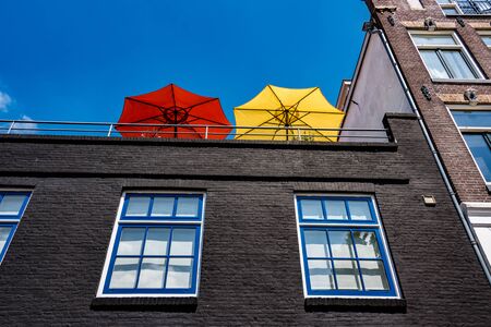 red and yellow parasols on a high balcony against blue above white and blue windowsの写真素材