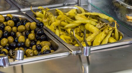 ingredients at a falafel bar with metal vegetable tongs green peppers black olives green olivesの写真素材