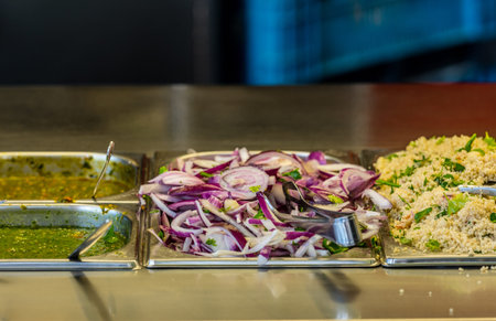 ingredients at a falafel bar with metal vegetable tongs onions, sauce rice