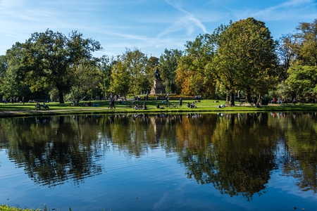 Amsterdam, Holland, August 2019 Reflections at Amsterdam Vondelpark during autumn with trees in beautiful colors reflecting in the water and a statue of Joost van den Vondelのeditorial素材