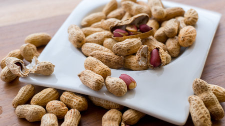 Peanuts in nutshell on a piece of wood and peeled peanuts in a white bowl