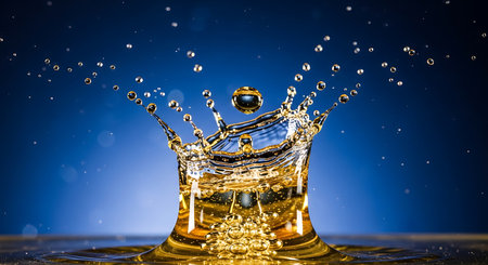 A mesmerizing water drop collision creates an artful liquid sculpture through high speed photography against blue backdropの素材