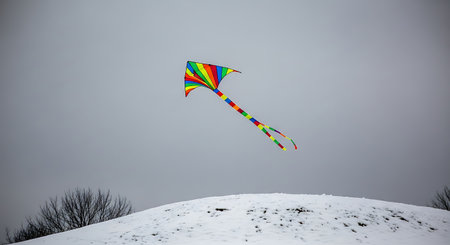 Bright kite flies above a snowy hill. Winter landscape and outdoor play. Recreation in simple color paletteの素材